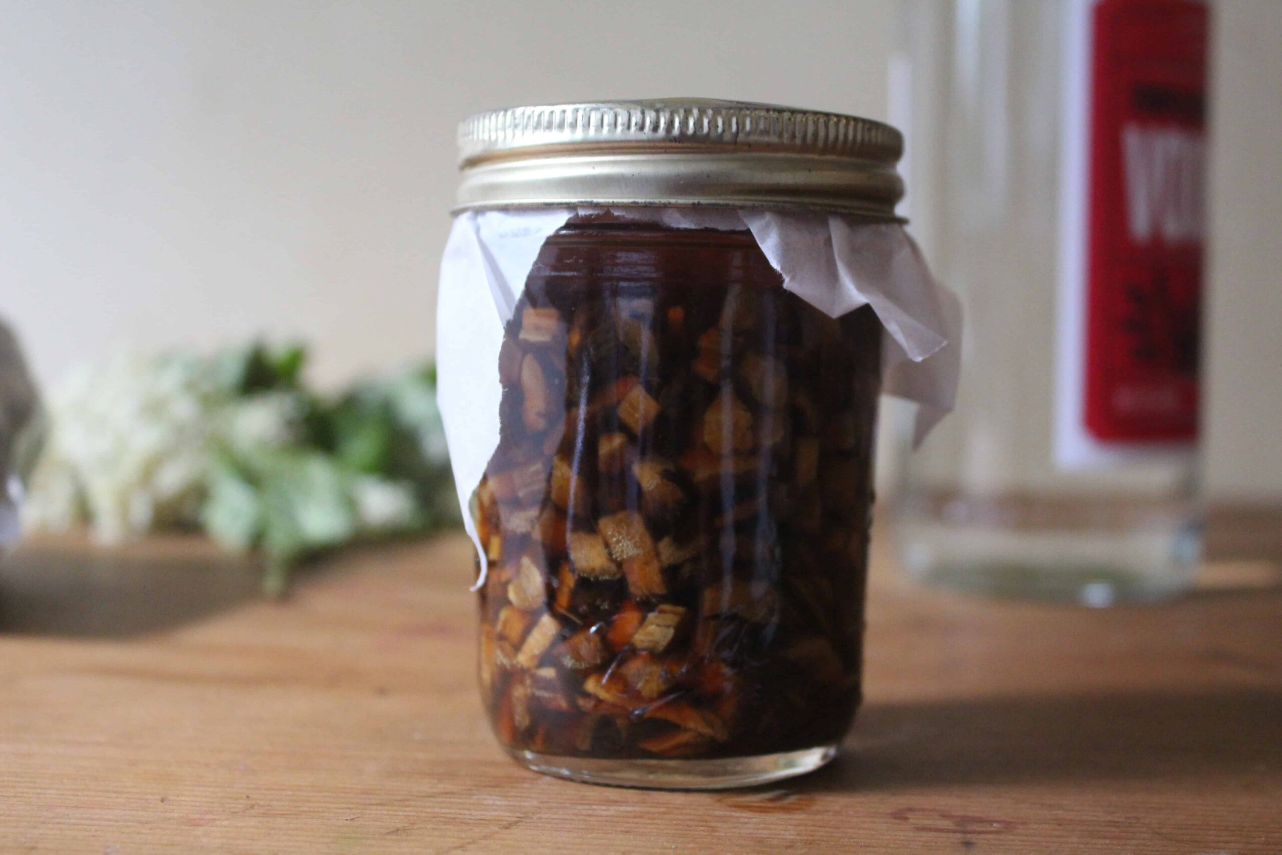 Dandelion roots steeping in alcohol in a small glass jar to make a tincture.