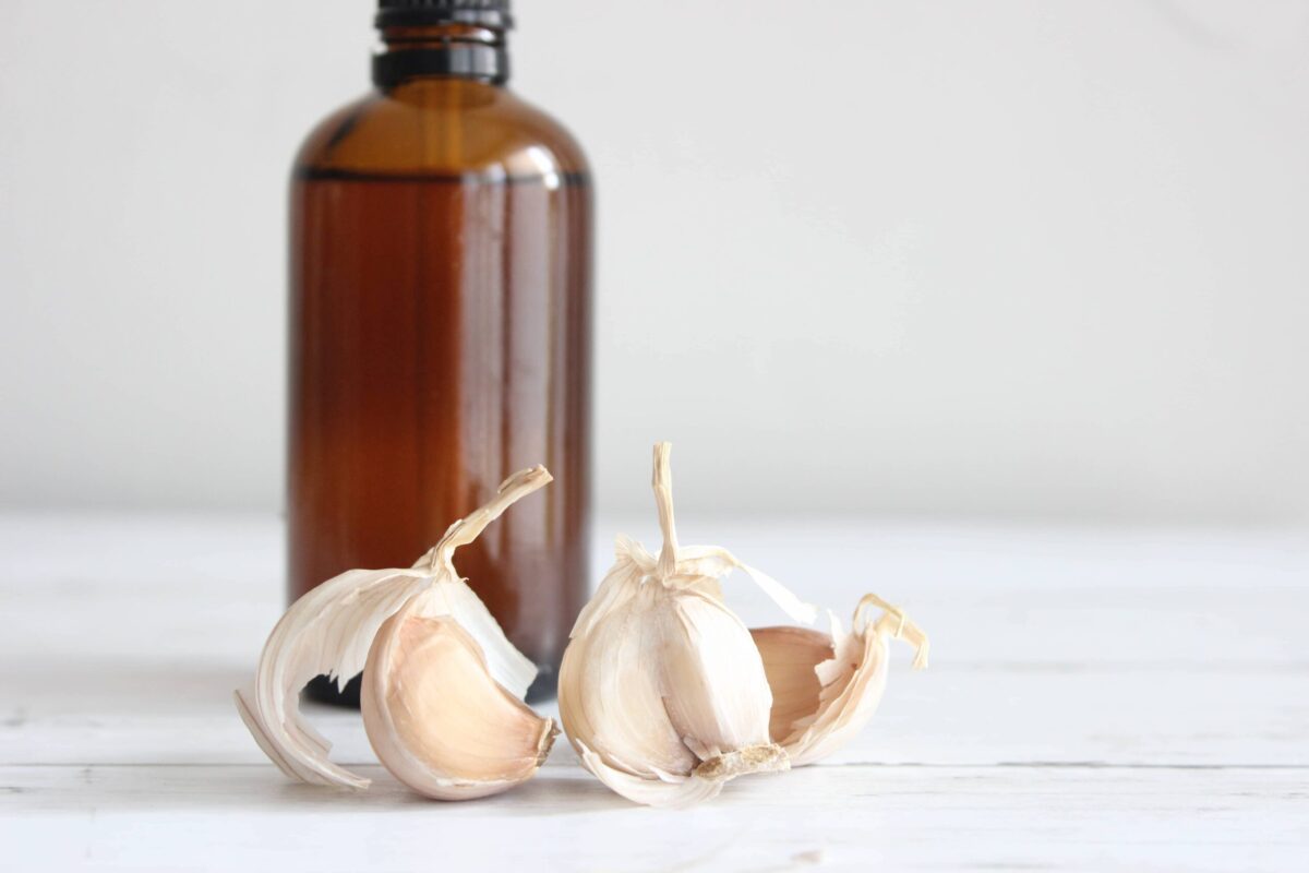 An amber glass bottle with garlic cloves in front of it.