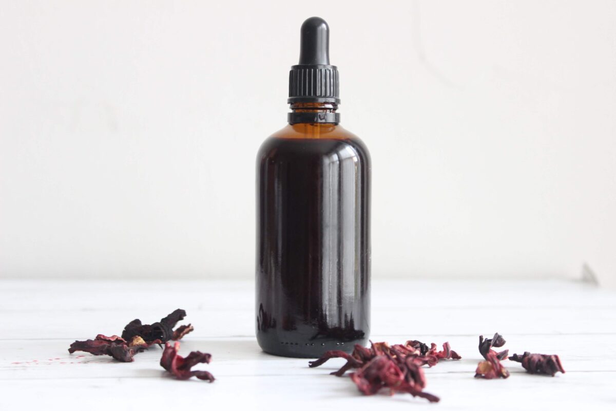 An amber glass dropper bottle with hibiscus tincture inside. There are dried hibiscus flowers around the bottle.