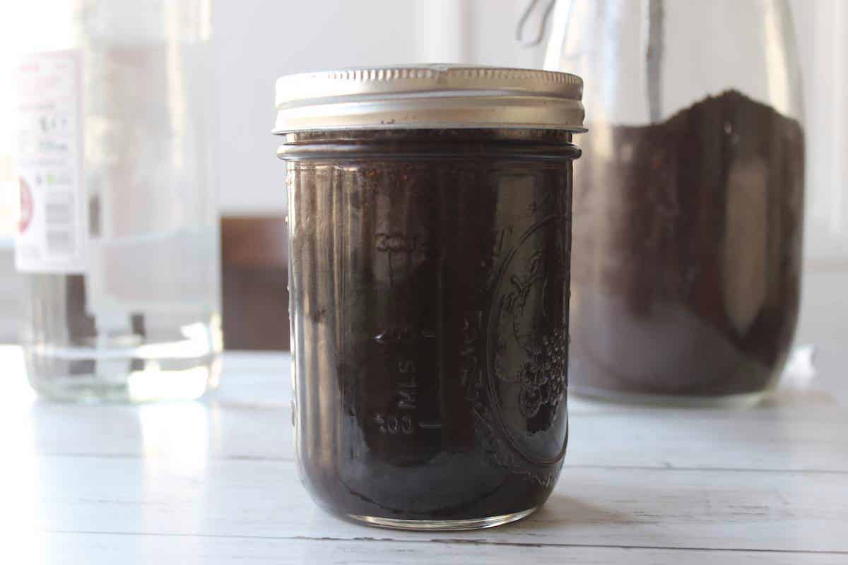 A glass jar with coffee extract steeping inside. There is a glass jar with gorund coffee in the background.