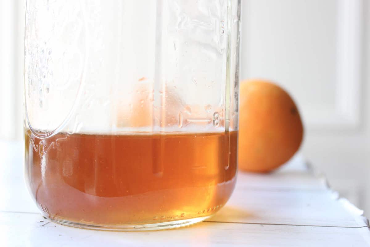 A close up of a glass jar with orange extract inside. There's a fresh orange behind the jar.