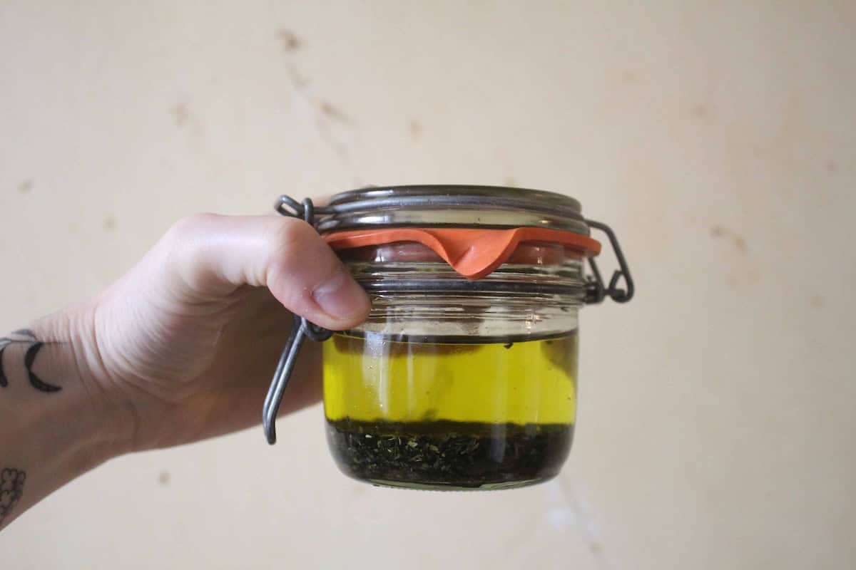 A light hand holding a glass jar with plantain steeping in oil.