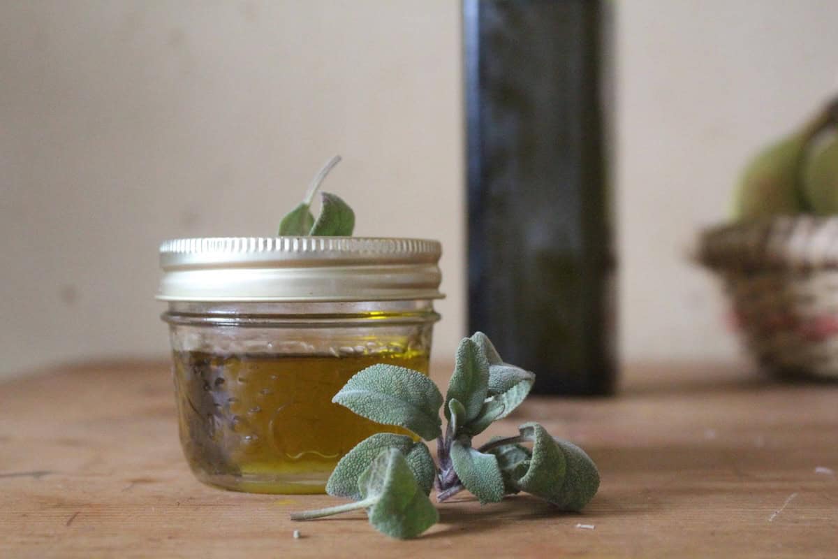 Fresh sage next to a small jar of sage infused olive oil. There's a green bottle of olive oil in the background.