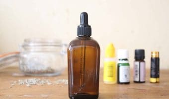 An amber glass dropper bottle with homemade face serum and essential oils in the background.