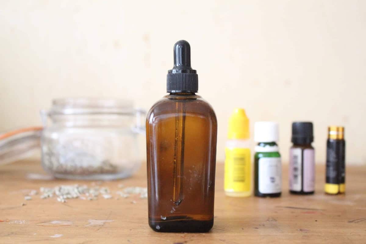 An amber glass dropper bottle with homemade face serum and essential oils in the background.
