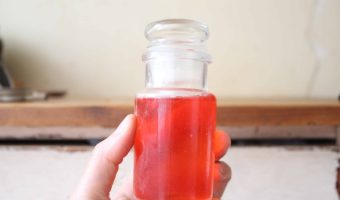 A hand holding a glass bottle with raspberry extract inside.