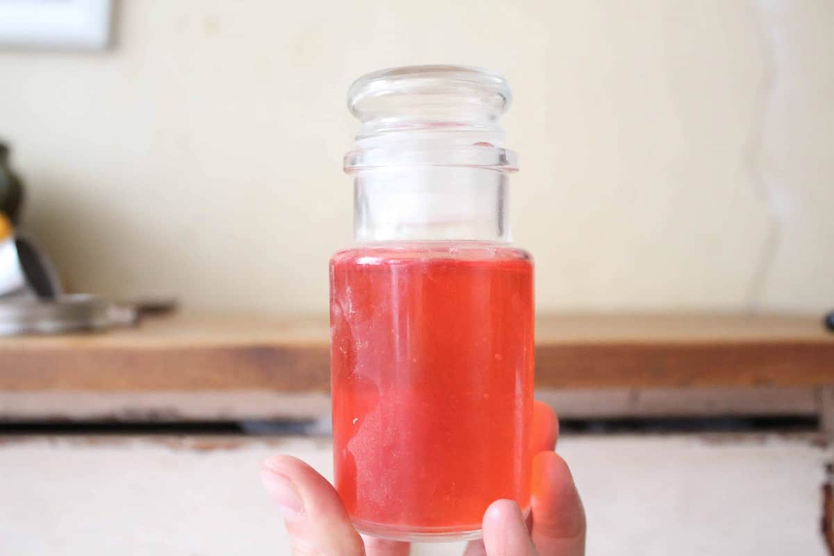 A hand holding a glass bottle with raspberry extract inside.
