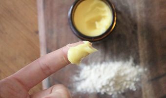 A close up of a finger with wild yam cream on it. There is a small jar of wild yam cream in the background. There is powdered wild yam beside the jar.