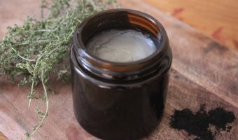 A close up of a homemade black drawing salve in an amber glass jar. There's activated charcoal next to is.