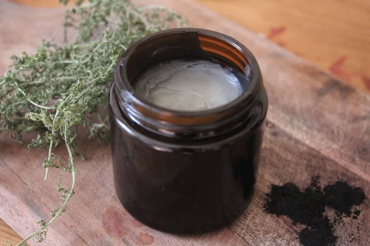 A close up of a homemade black drawing salve in an amber glass jar. There's activated charcoal next to is.